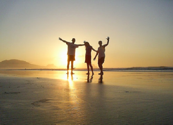 Imagem do pôr do sol e três pessoas caminhando felizes na praia