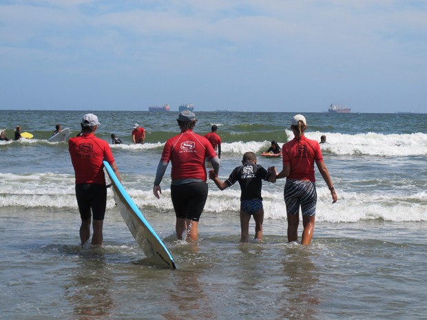 Professores e Raphael entram no mar para uma aula de surfe (Foto: Mariane Rossi/G1)